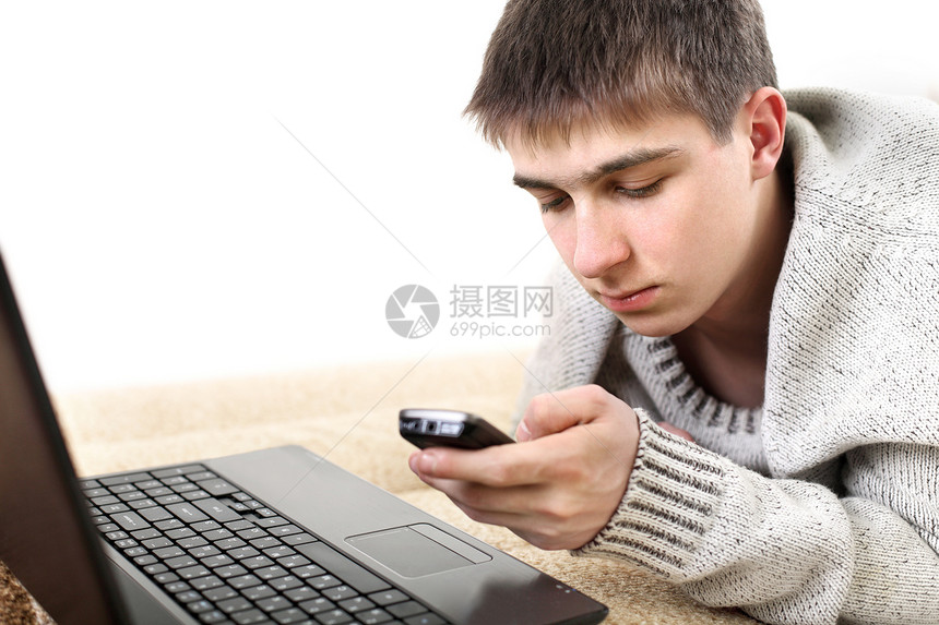 拥有笔记本和电话的青少年说谎游戏男生男性白色交易互联网沙发毛衣细胞图片