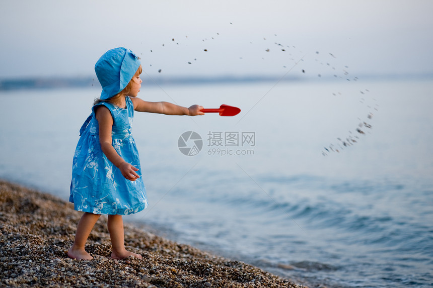 海滩上的小女孩衣服蓝色石头海浪女性童年场景快乐赤脚卵石图片