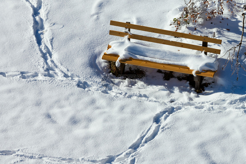 雪地覆盖公园长凳周围的雪脚印图片