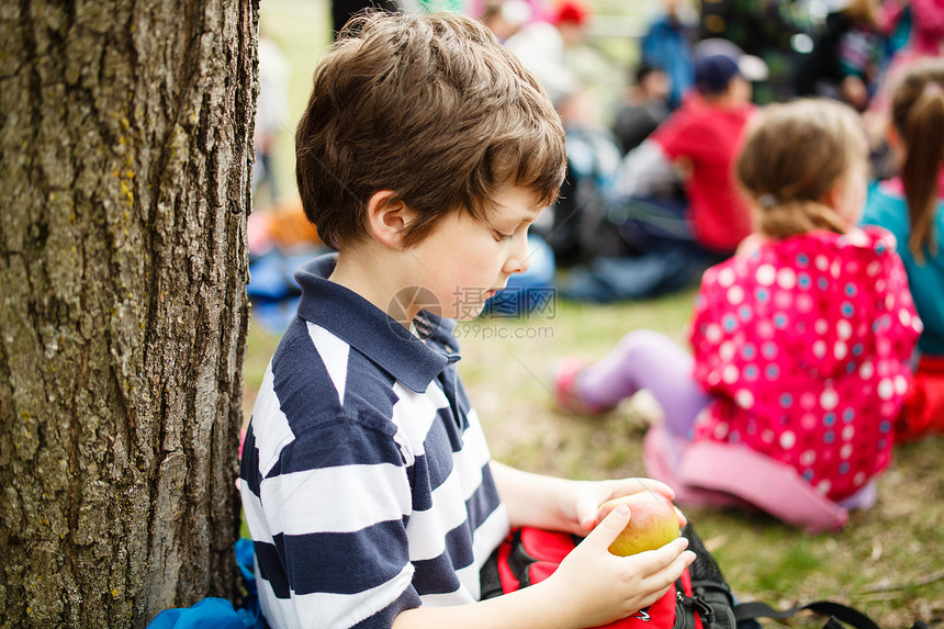 男孩坐在树旁旅行童年男性男生学校休息食物孩子们场地背包图片