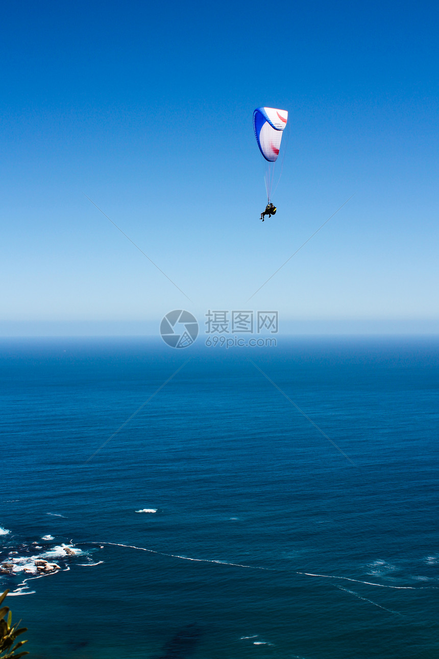 在蓝天空和蓝水前飞行的滑翔伞图片