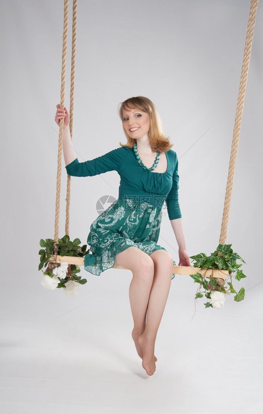 在秋千上穿绿裙子的美女青少年花朵绿色若虫魅力头发微笑绳索座位金发图片