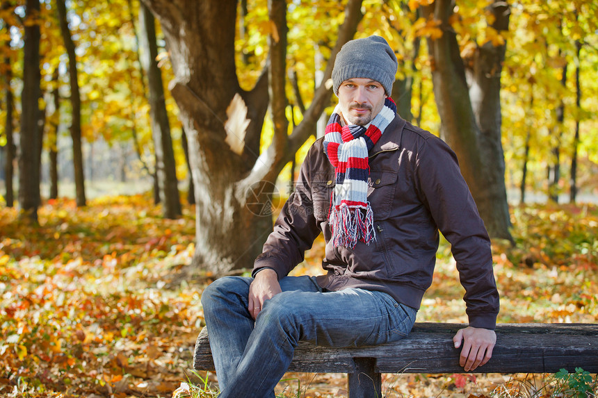 秋天公园里的男人乐趣太阳微笑男性公园长椅青年帽子树叶蓝色图片
