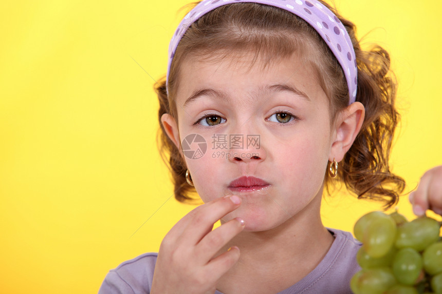 小女孩吃着一捆绿葡萄图片