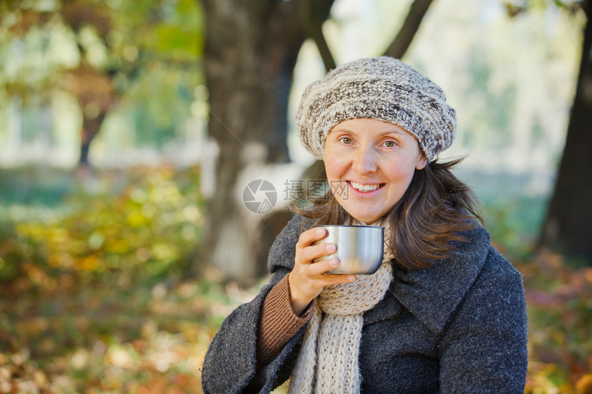 女人在秋天公园喝茶微笑太阳外套乐趣杯子女性公园围巾女孩青年图片