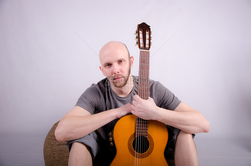 拿着吉他光秃秃的好人头发音乐岩石吉他手男性玩家帽子音乐会牛仔裤生活图片