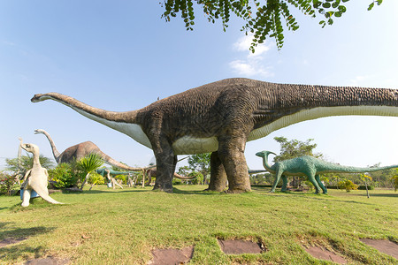 雕像和恐龙公共公园侏罗纪捕食者化石爬虫公园公共公园恐龙蓝色天空艺术背景图片