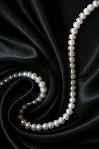 黑色丝绸上的白珍珠作为背景魅力珠子象牙光泽度项链女性宝藏珠宝细绳反射背景图片