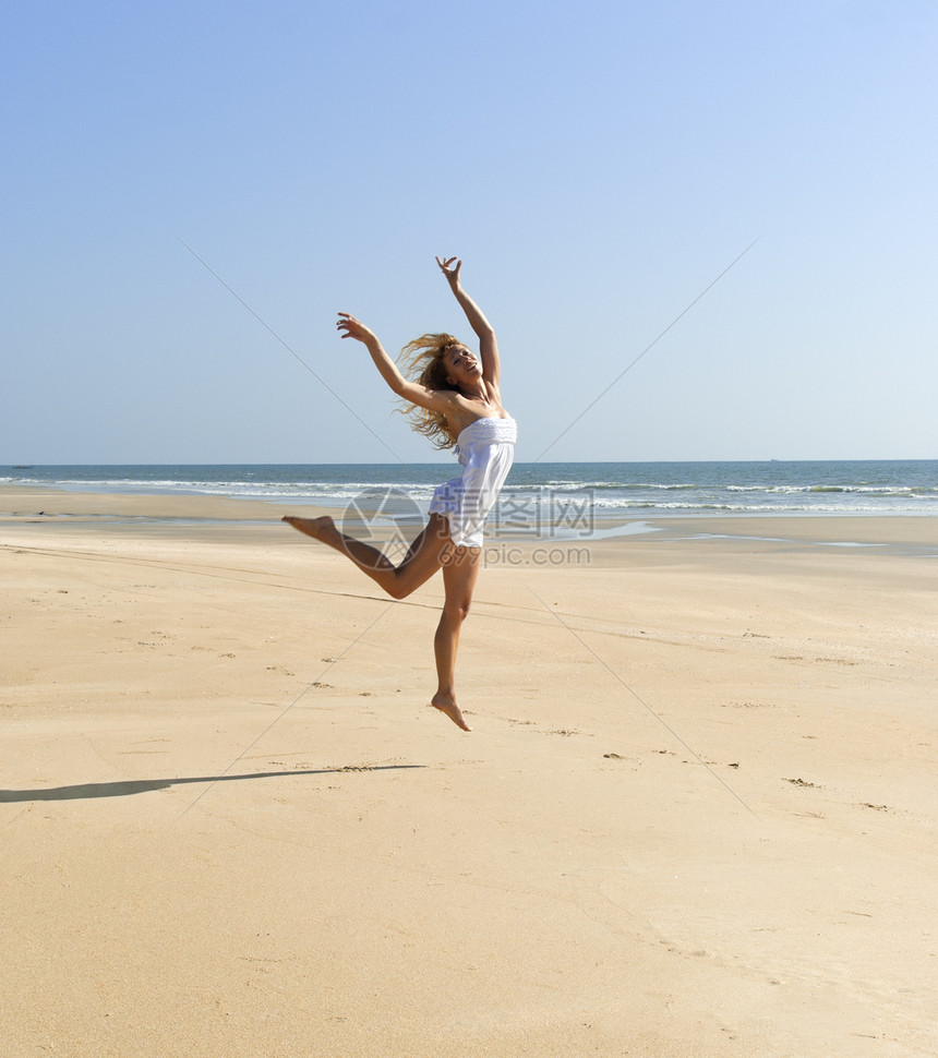 快乐的女人跳上阳光明媚的海滩图片