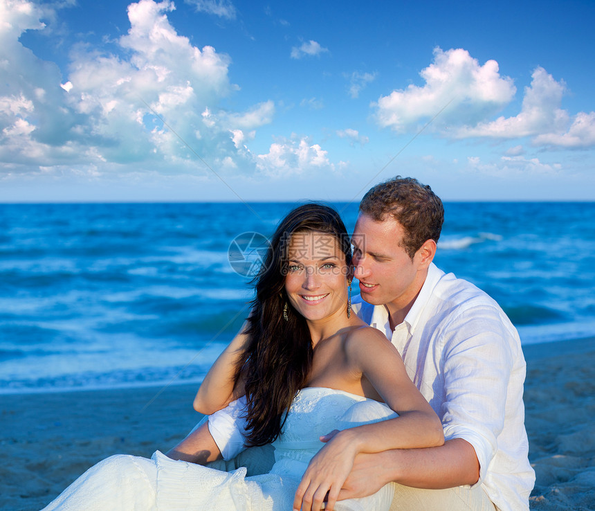 在蓝沙滩上坐着丈夫幸福男人假期婚姻女性夫妻蓝色波浪婚礼图片