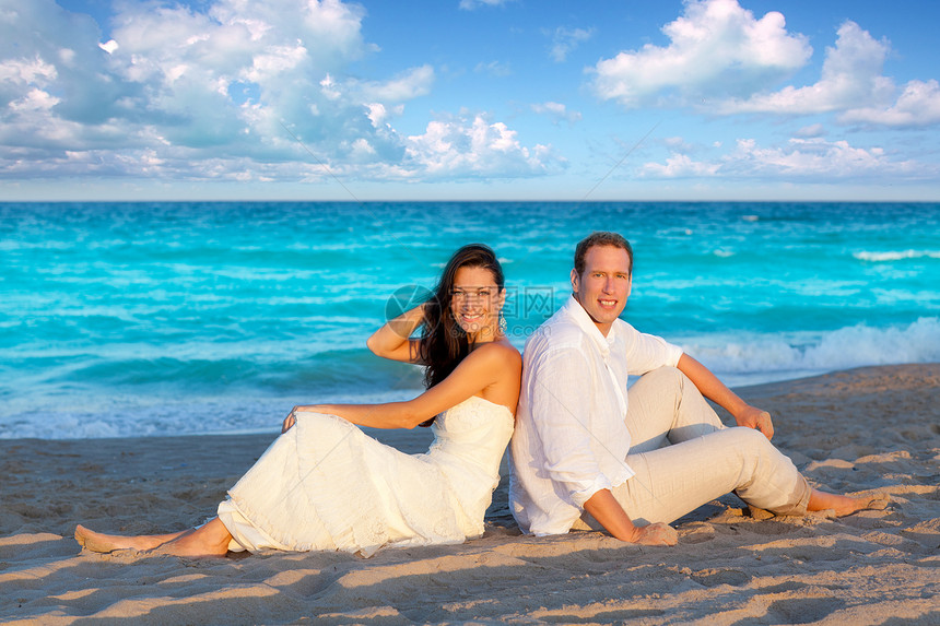 在蓝沙滩上坐着支撑天空假期裙子蜜月庆典波浪海滩婚姻海洋图片