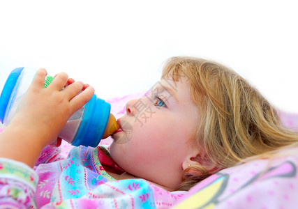女孩在床上喝着一瓶牛奶童年饮料瓶子枕头液体金发女性眼睛营养蓝色美丽的高清图片素材