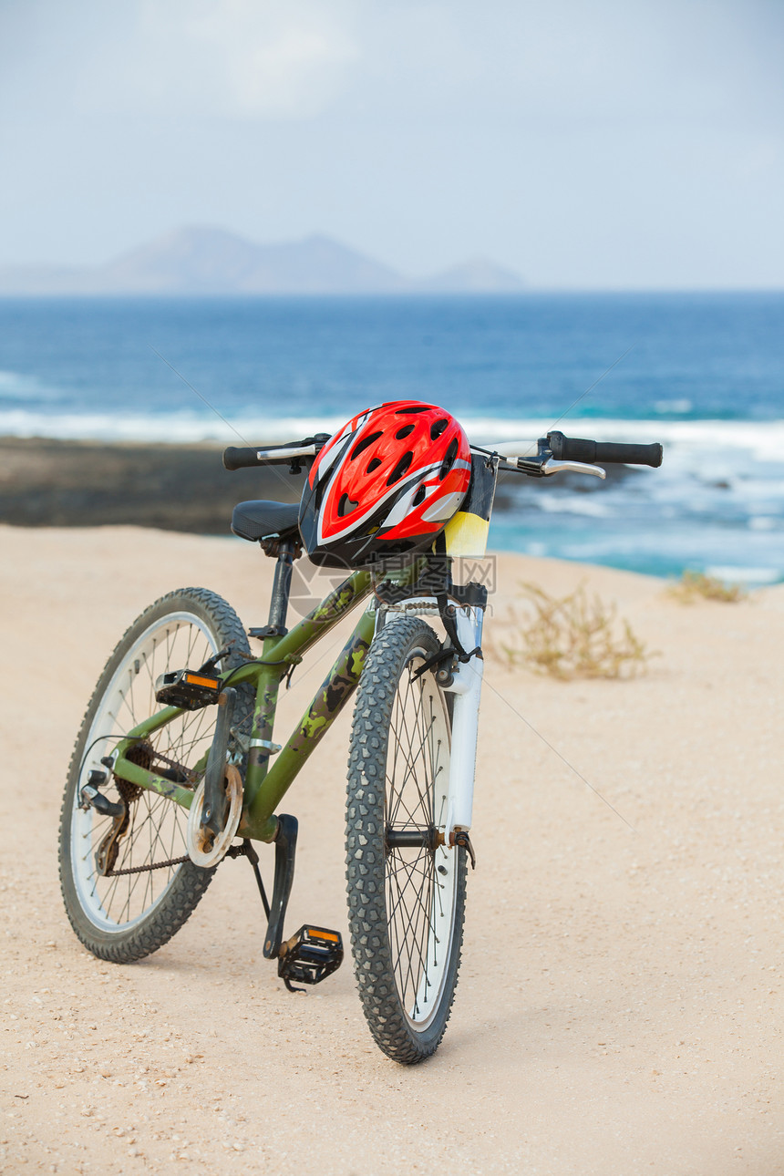 骑着头盔的自行车 站在海滩上浮木运动冒险阴影娱乐蓝色旅行海岸海洋戏剧性图片