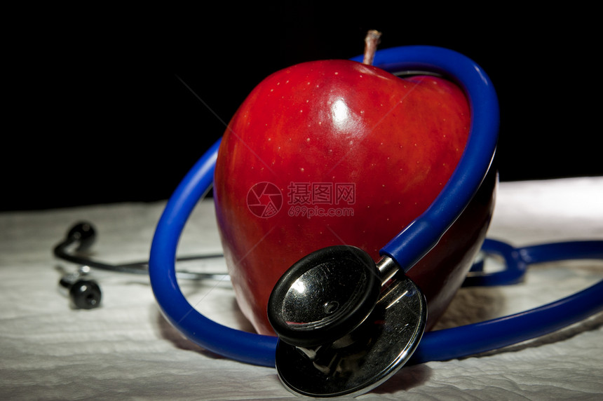 由蓝色医学听诊器包围的放大苹果图片