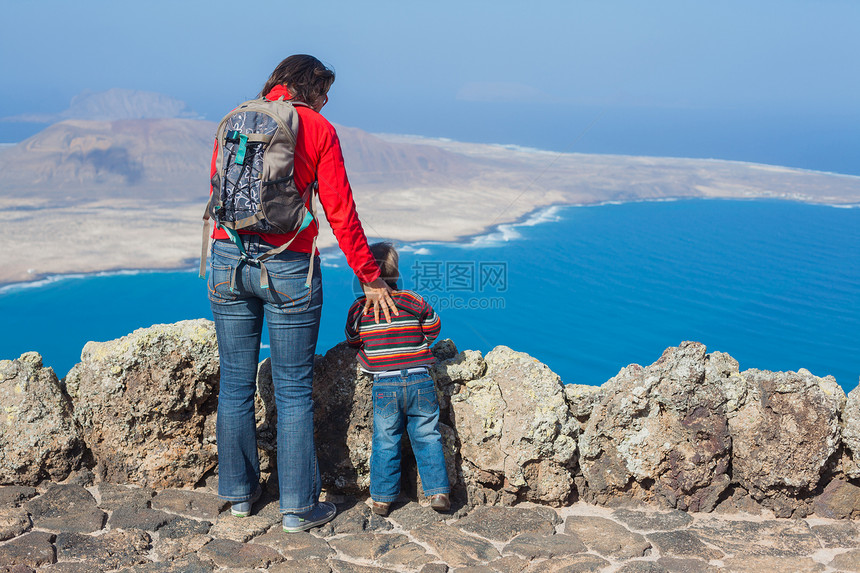 看着母亲和儿子站在悬崖边缘的背面男生石头公园背包高度旅行闲暇游客阳光冒险图片