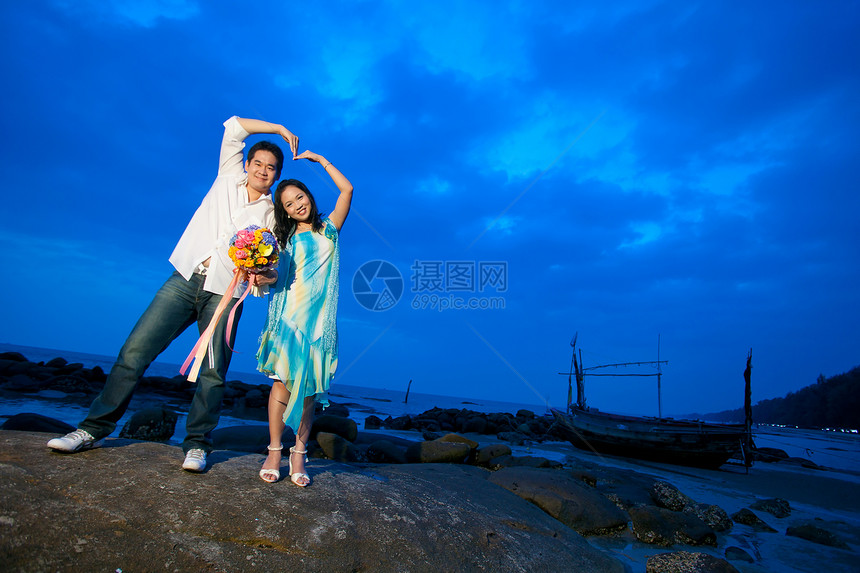 年轻夫妇在沙滩上做心脏标志幸福妻子喜悦女孩享受丈夫花朵纽带男人订婚图片