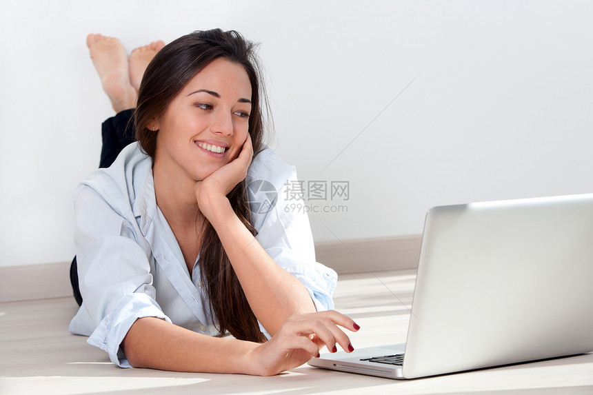 年轻妇女用笔记本电脑躺在地板上图片