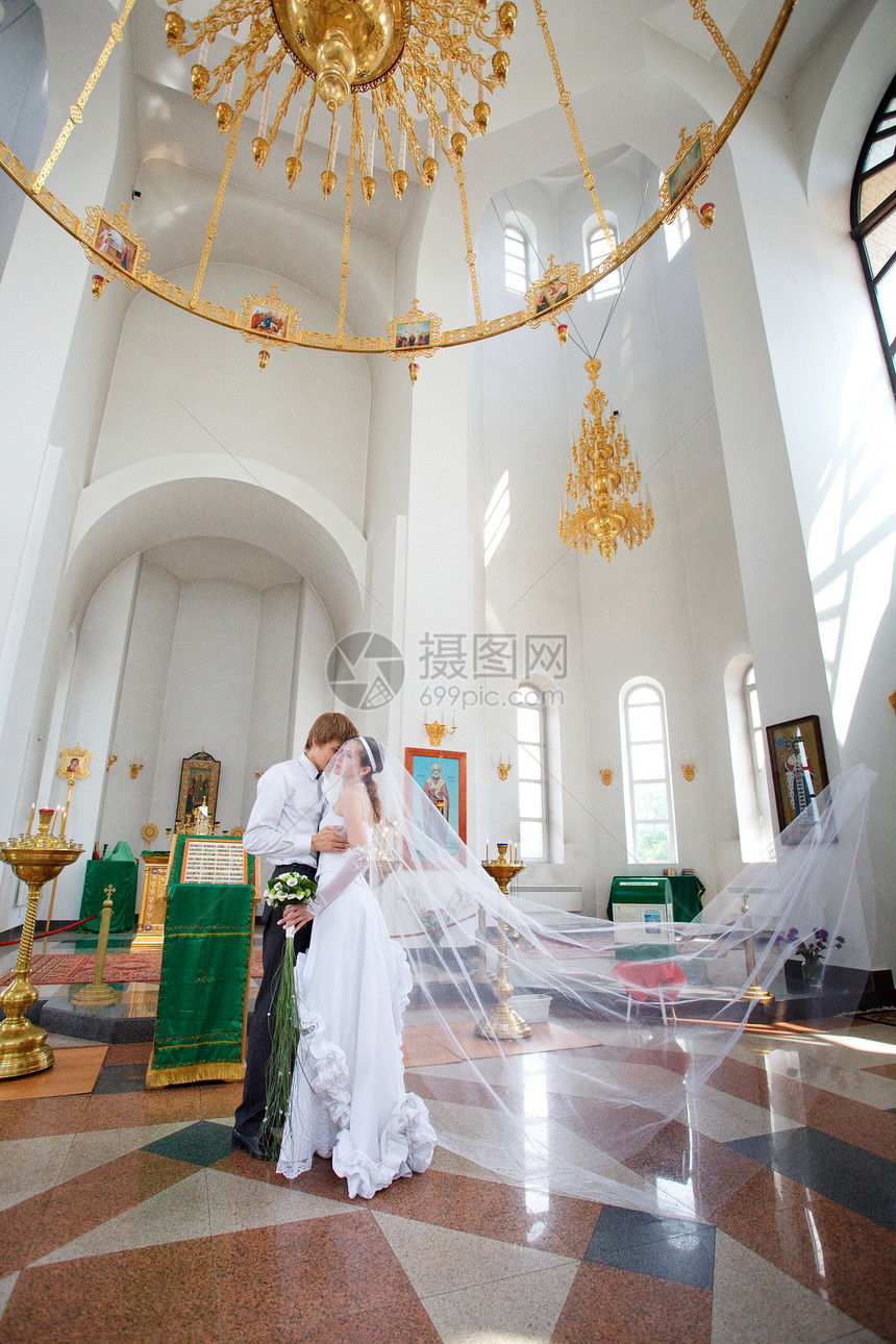 教堂中的新娘和新郎寺庙仪式枝形吊灯精神信仰婚礼墙壁男性花束图片