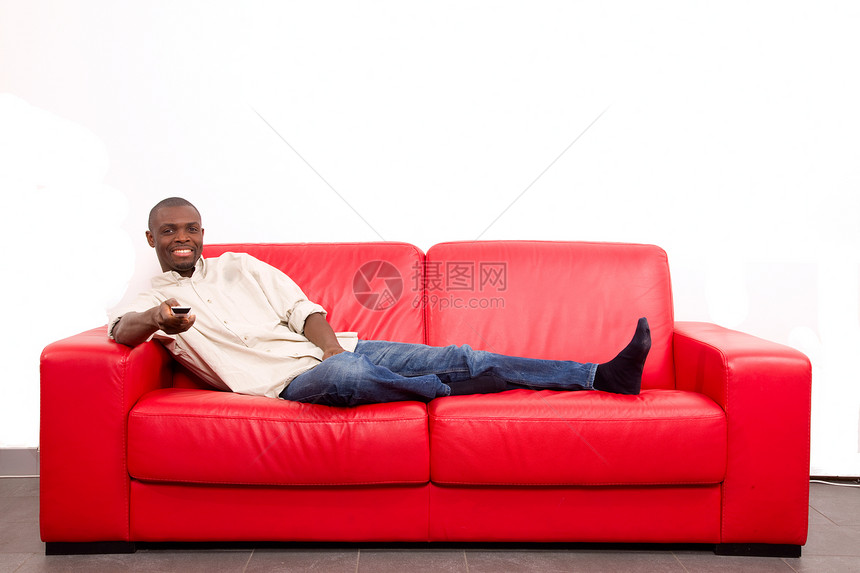 在沙发上用遥控器的人牛仔裤休闲装男人商务家具遥控手势红色人士闲暇图片