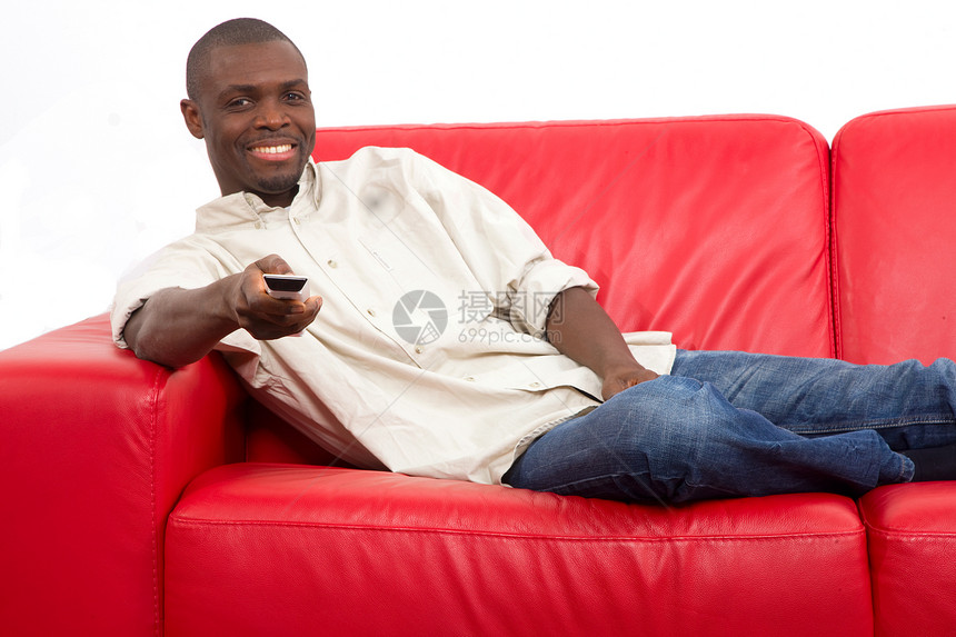 在沙发上用遥控器的人家具男人红色商务人士闲暇微笑休闲装手势牛仔裤图片