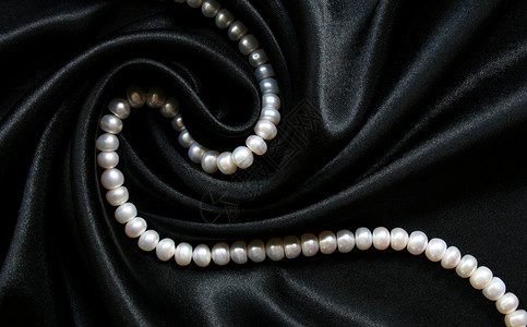 黑色丝绸上的白珍珠作为背景宝石宝藏细绳奢华女性手镯礼物光泽度反射展示背景图片