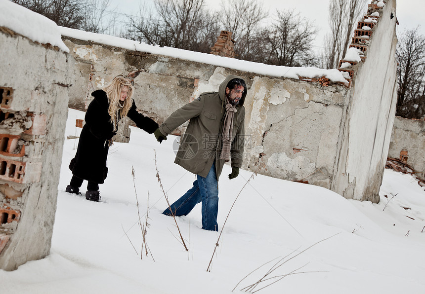 无家可归的一对夫妇在雪中举手牵手行走图片