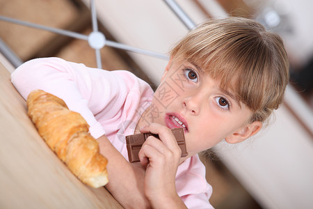 咬一口的巧克力带羊角面包和巧克力棒的年轻女孩背景