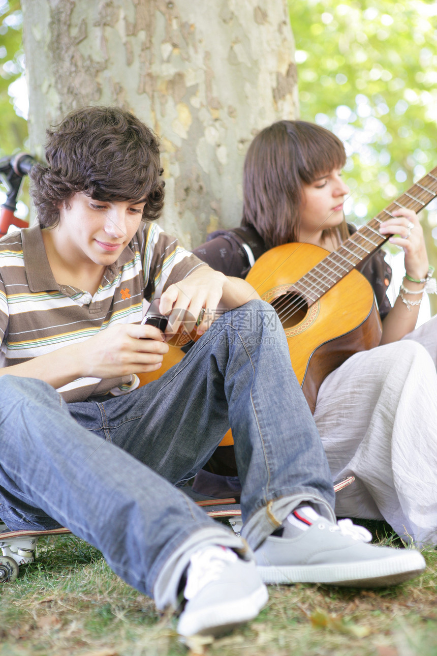 两个十几岁的吉他手坐在树边图片