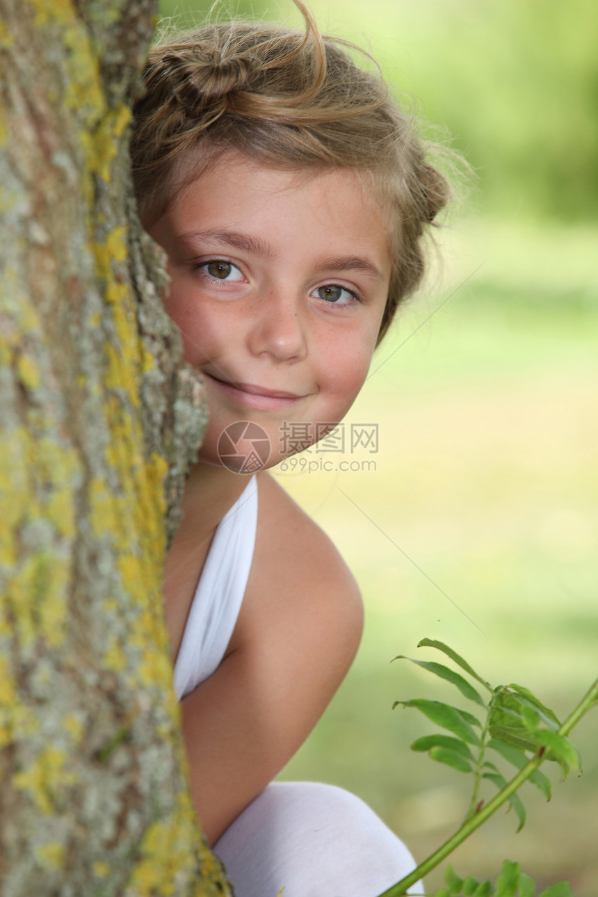 身着白色衣服的年轻女孩躲在树后面图片