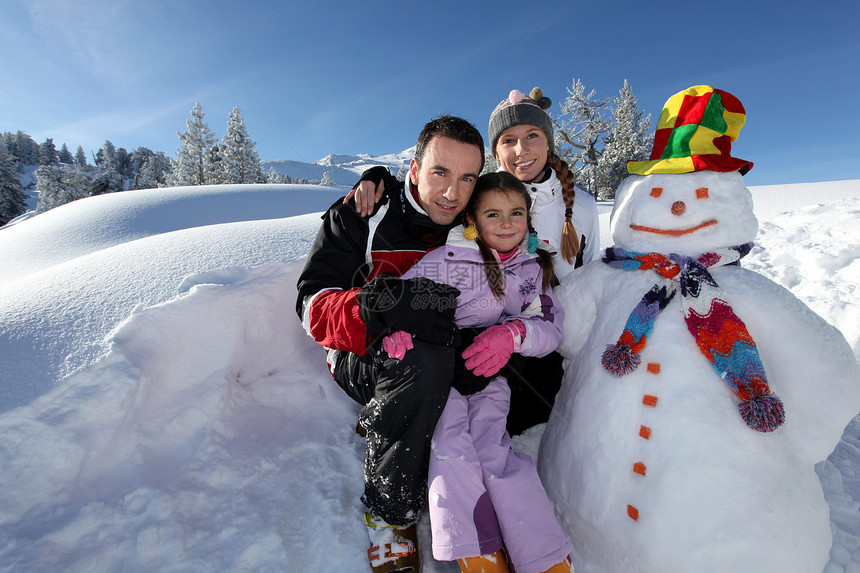 在山地度假胜地雪人旁边与孩子一起玩耍的情侣图片