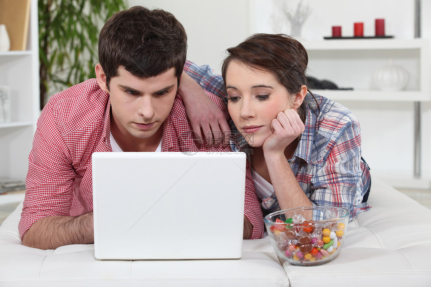 在家使用笔记本电脑的年轻夫妇长椅电子邮件沙发成年人甜心喜悦男朋友青少年微笑技术图片