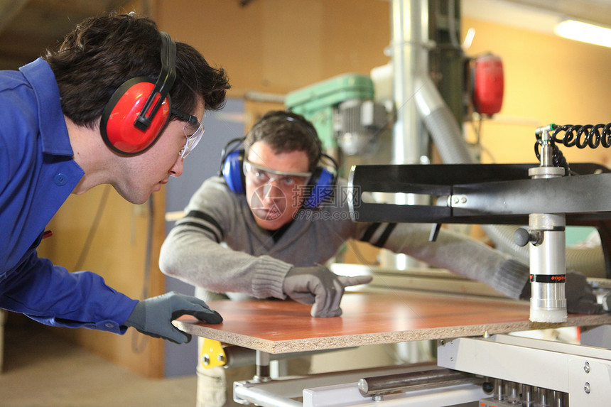 一名经验丰富的工人 展示学徒如何使用机器切割一块木柴;该名工人图片