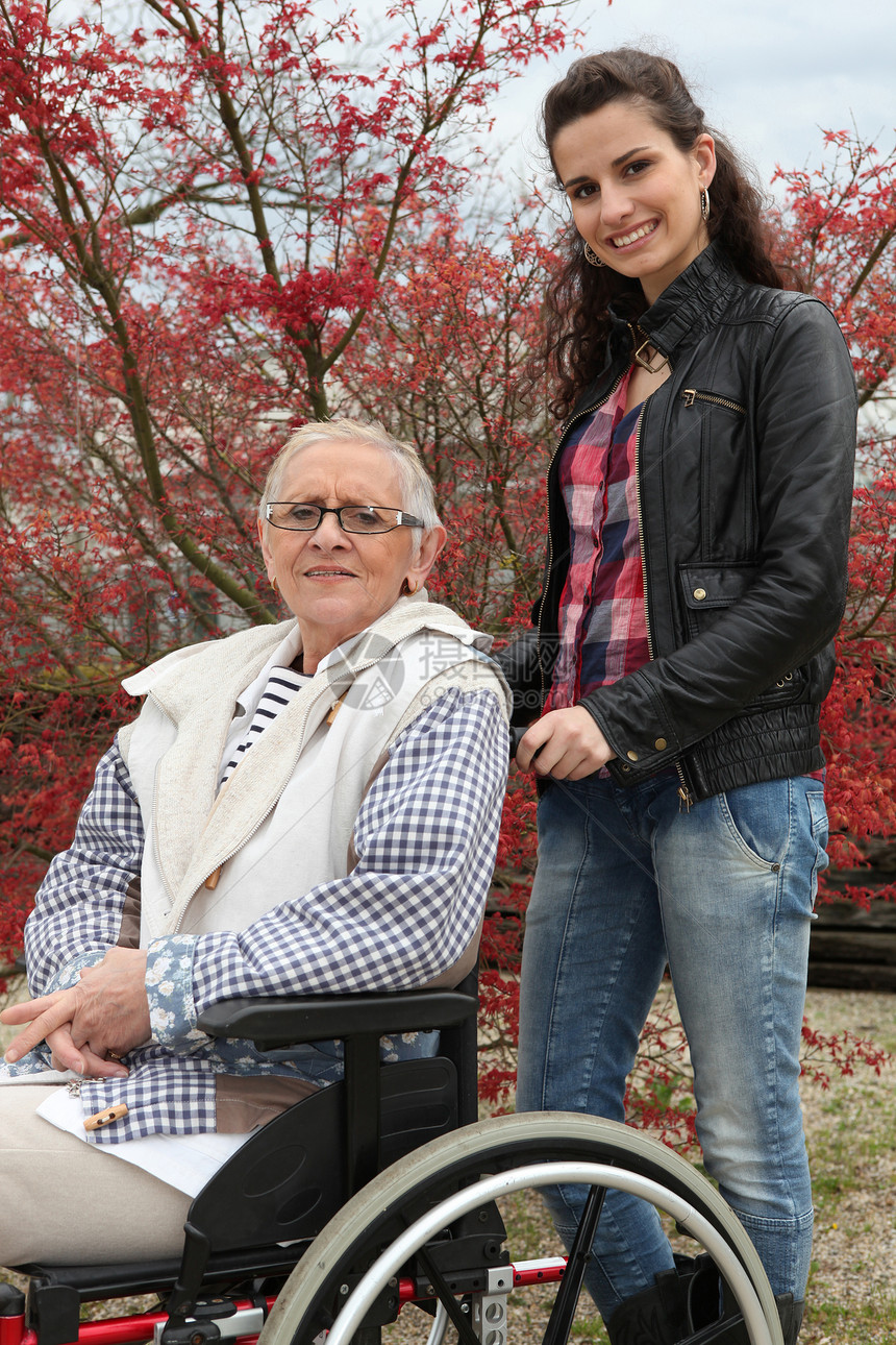 青年妇女推拉一名坐轮椅的老年妇女孙女轮缘疾病残障公园人士女性祖母花园辐条图片