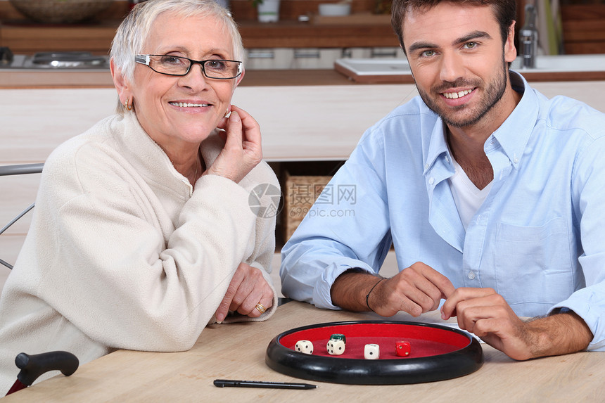 青年男子与年长妇女玩骰子团结桌子友谊帮助男人女士游戏个人服务工作图片