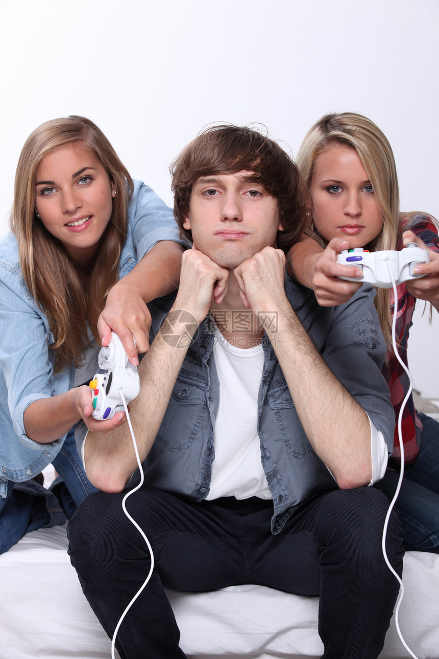 在两个玩电子游戏的朋友之间坐着的波尔十几岁青少年图片
