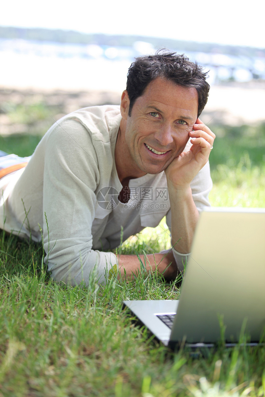 人笑着在草地上工作男性说谎笔记本微笑白色电脑头发男人棕色公园图片