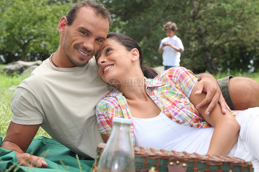 年轻夫妇和小男孩在背景中野餐的情侣图片