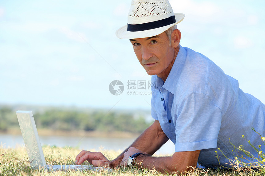 在笔记本电脑前躺在草地上的老人图片