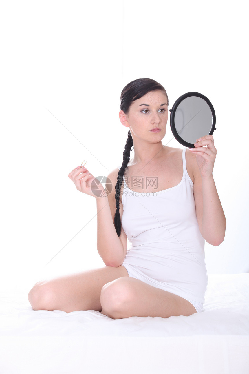 年轻女士坐在床上照着镜子图片