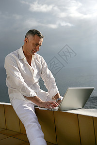 矮墙在海边的笔记本电脑上工作的人背景
