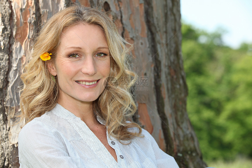 在树干旁边坐着 头发上花朵的夏月女人图片