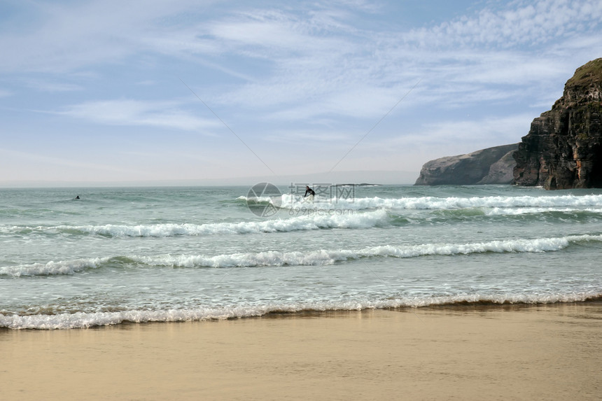在球状悬崖附近冲浪的冲浪者力量蓝色闲暇波浪男人岩石娱乐海浪海滩海洋图片