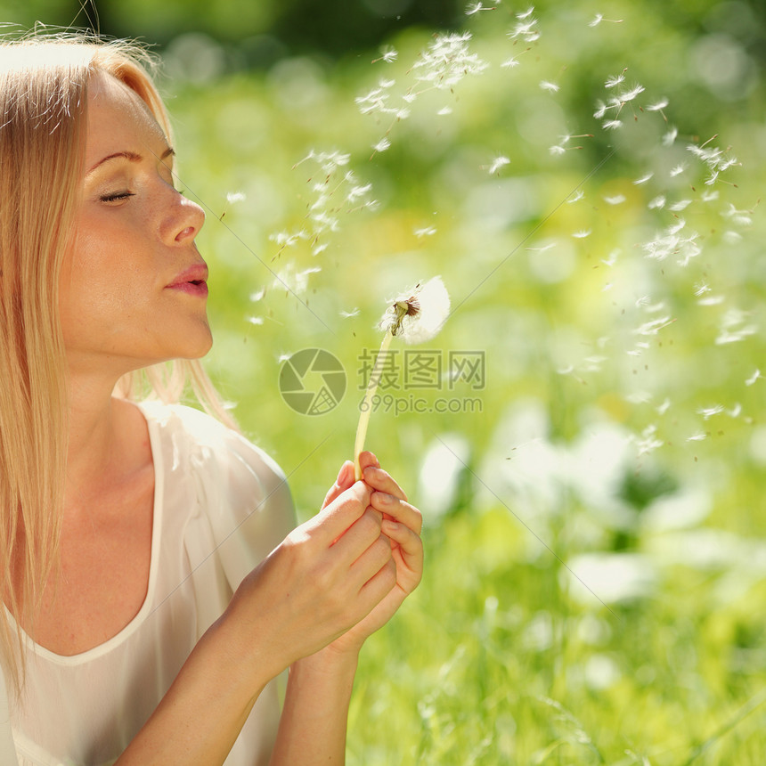 女孩吹在花朵上金发女郎快乐享受嘴唇植物头发微笑女性自由乐趣图片