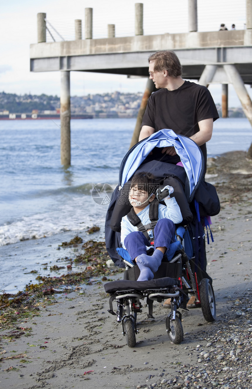 父亲在海滩上和残疾儿子一起推轮椅图片