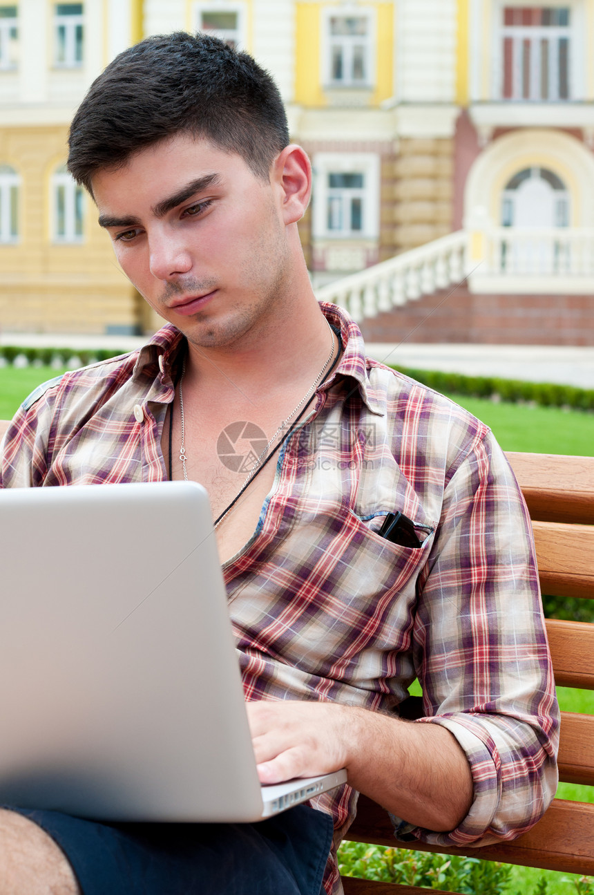 年轻人坐在长椅上 在笔记本电脑上工作图片