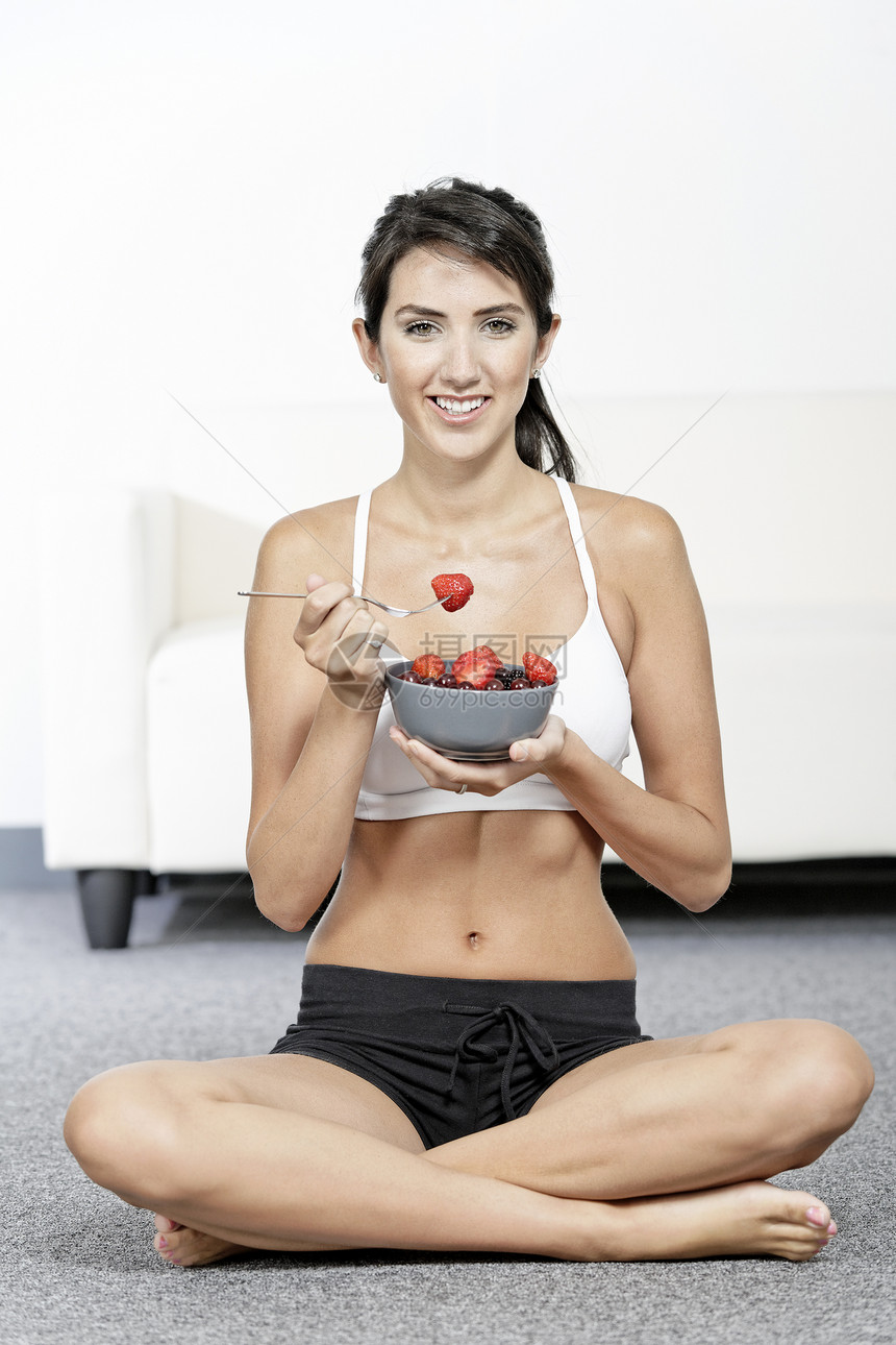 女性在健身衣着中吃水果生活背心女士短裤双肩健康饮食浆果饮食快乐微笑图片