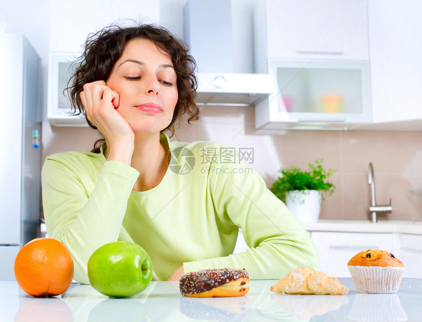 美丽的年轻女子在水果和甜甜之间选择食物诱惑巧克力午餐损失碳水身体蛋糕桌子垃圾厨房图片