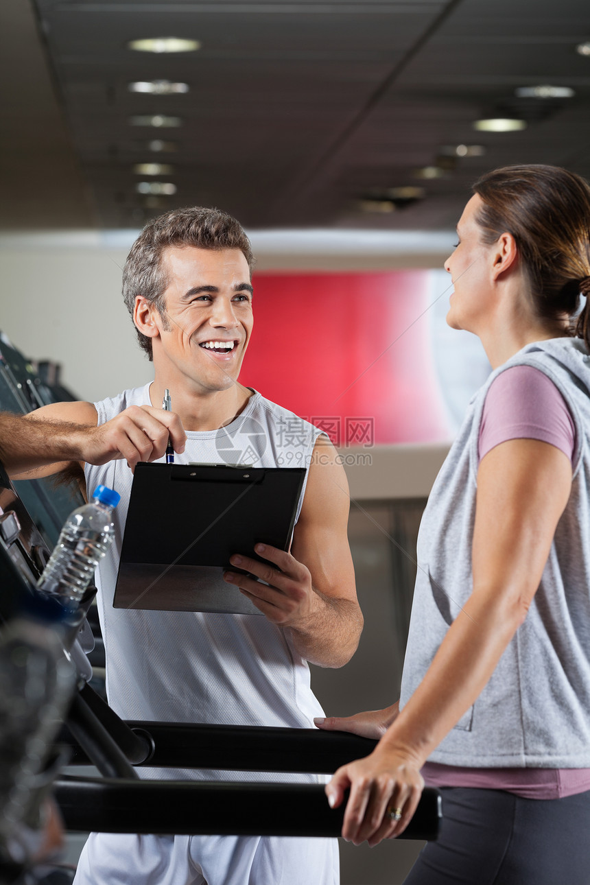快乐的教官在Treadmill上观看客户对客户进行Expercising图片