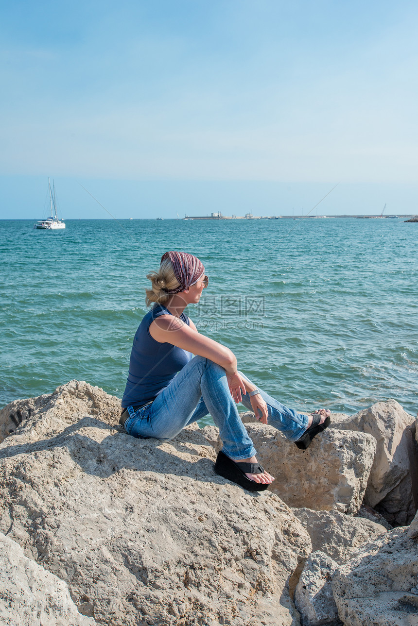 坐在岩石上看着地中海海的年轻女士们 坐落在岩石上图片