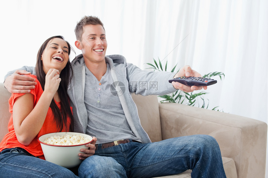 一对欢笑的情侣 享受着电视秀 当他们吃流行口感时图片